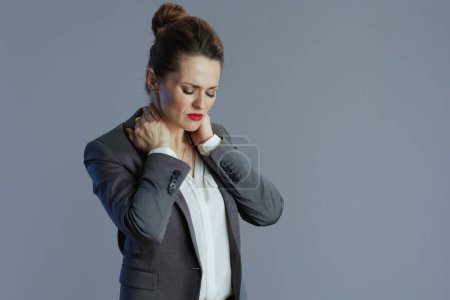 Foto de Estresado elegante 40 años de edad mujer de negocios en traje gris con dolor de cuello contra fondo gris. - Imagen libre de derechos
