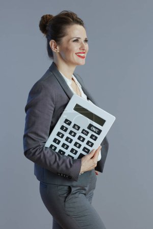 Photo for Happy 40 years old business woman in gray suit with calculator isolated on grey background. - Royalty Free Image