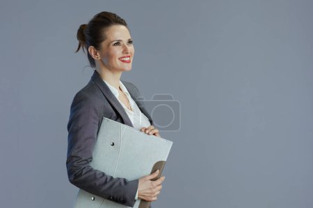 Téléchargez les photos : Souriant tendance 40 ans femme travailleur en costume gris avec dossier isolé sur fond gris. - en image libre de droit