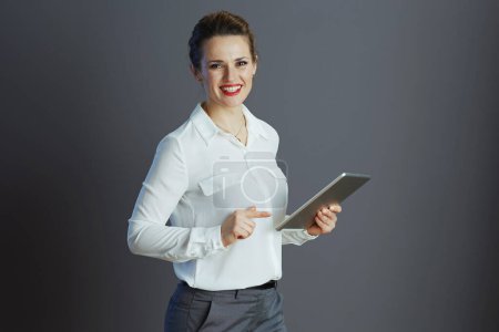 Foto de Sonriente trabajadora femenina de moda en blusa blanca con tablet PC sobre fondo gris. - Imagen libre de derechos