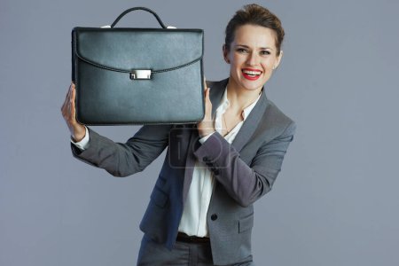 Foto de Feliz moderno 40 años de edad, mujer trabajadora en traje gris con maletín sobre fondo gris. - Imagen libre de derechos