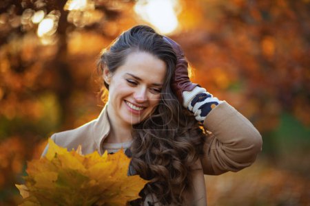 Photo for Hello september. smiling young woman in beige coat with autumn yellow leaves outdoors on the city park in autumn. - Royalty Free Image