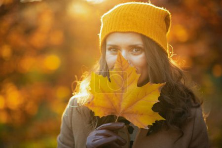 Foto de Hola otoño. elegante mujer de 40 años en abrigo beige y sombrero naranja que se esconde detrás de la licencia amarilla de otoño al aire libre en el parque de la ciudad en otoño. - Imagen libre de derechos
