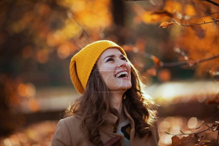 Téléchargez les photos : Bonjour septembre. Femme élégante et souriante en manteau beige et chapeau orange à l'extérieur dans le parc de la ville en automne. - en image libre de droit
