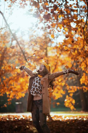 Photo for Hello september. happy elegant middle aged woman in beige coat and orange hat rejoicing outdoors on the city park in autumn. - Royalty Free Image