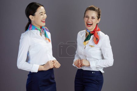 Téléchargez les photos : Souriant élégant hôtesse de l'air femmes en jupe bleue, chemise blanche et écharpe sur fond gris. - en image libre de droit