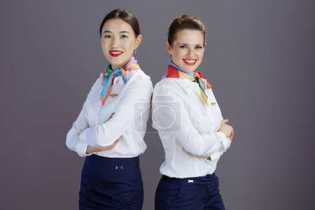 Foto de Retrato de las asistentes de vuelo modernas felices en falda azul, camisa blanca y bufanda aislada sobre fondo gris. - Imagen libre de derechos