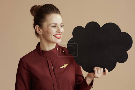 Photo for Smiling modern flight attendant woman against beige background with cloud shaped blackboard. - Royalty Free Image