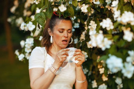 Photo for Summer time. sad stylish female in white shirt with handkerchief has an allergy attack near flowering tree. - Royalty Free Image