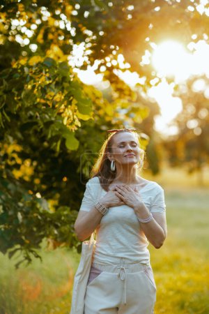 Foto de Hora de verano. mujer elegante sonriente en camisa blanca con la mano en el pecho fuera en la naturaleza. - Imagen libre de derechos
