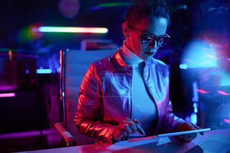 Téléchargez les photos : Neon metaverse concept futuriste. femme élégante dans les lunettes en utilisant tablette PC dans le bureau moderne. - en image libre de droit