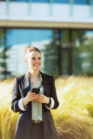 Photo for Happy modern woman worker near business center in black jacket using smartphone. - Royalty Free Image
