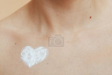 Foto de Primer plano en la mujer de mediana edad con crema en forma de corazón en el pecho. - Imagen libre de derechos