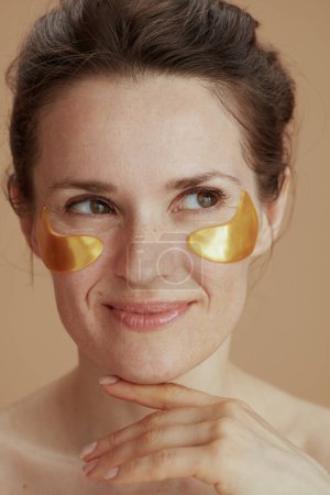 Photo for Smiling middle aged woman with eye patches isolated on beige background. - Royalty Free Image