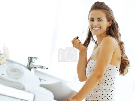 Photo for Happy young woman with lip gloss in bathroom - Royalty Free Image
