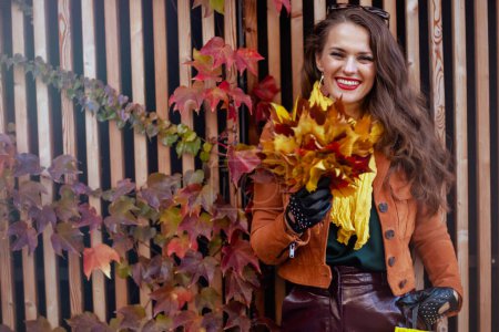 Foto de Hola noviembre. mujer elegante feliz en gabardina marrón con hojas amarillas de otoño en la ciudad. - Imagen libre de derechos