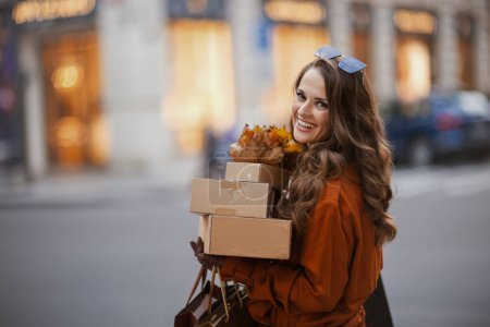 Foto de Hola noviembre. joven sonriente en gabardina marrón con parcelas, bolsas de compras y hojas amarillas de otoño en la ciudad. - Imagen libre de derechos