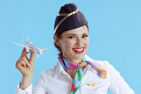 Photo for Happy modern female air hostess on blue background in uniform with a little airplane. - Royalty Free Image