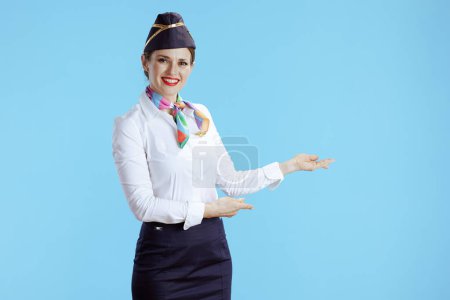 Photo for Smiling modern female air hostess against blue background in uniform welcoming. - Royalty Free Image