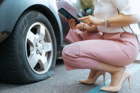 Photo for Car accident. Closeup on tourist woman in the city with smartphone near car with flat tire. - Royalty Free Image