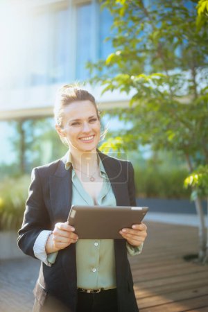 Foto de Feliz mujer de negocios moderna de mediana edad cerca del centro de negocios en chaqueta negra con tableta digital. - Imagen libre de derechos