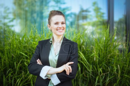 Téléchargez les photos : Portrait d'heureuse femme moderne de 40 ans employée près du centre d'affaires en veste noire avec bras croisés. - en image libre de droit