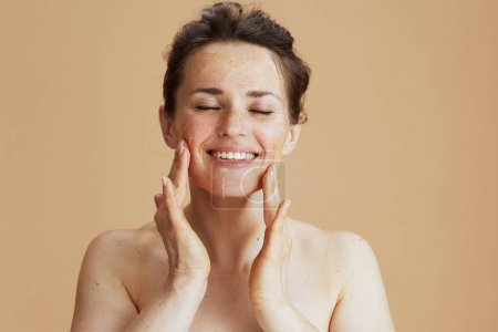 Foto de Sonriente mujer moderna de 40 años con exfoliante facial sobre fondo beige. - Imagen libre de derechos