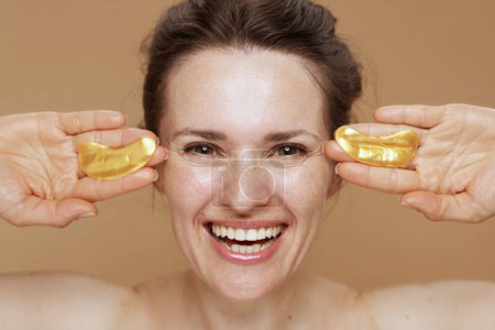 Téléchargez les photos : Heureuse femme moderne avec des patchs pour les yeux isolés sur fond beige. - en image libre de droit