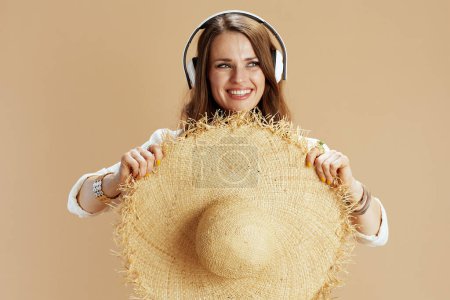 Photo for Beach vacation. smiling trendy woman in white blouse and shorts isolated on beige background listening to the music with headphones. - Royalty Free Image