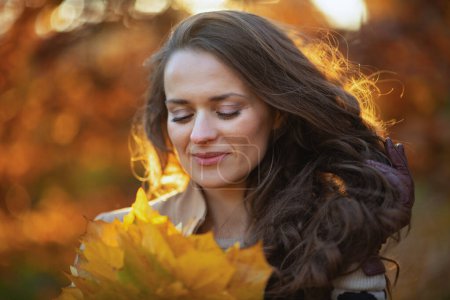 Foto de Hola otoño. relajado elegante mujer de 40 años de edad en abrigo marrón con hojas de color amarillo otoño al aire libre en el parque de la ciudad en otoño. - Imagen libre de derechos