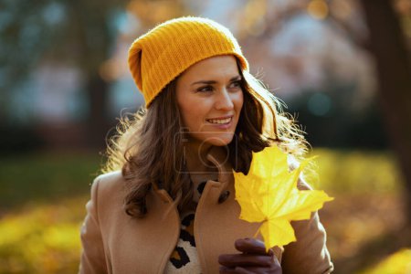 Photo for Hello october. happy trendy woman in beige coat and orange hat with autumn yellow leaves outdoors in the city in autumn. - Royalty Free Image