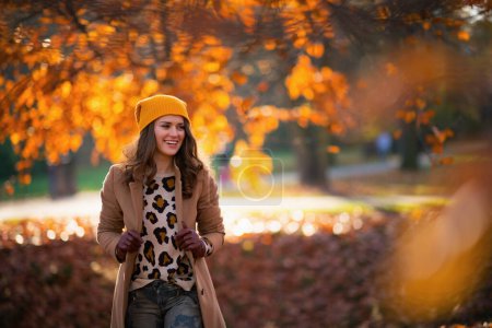 Photo for Hello november. smiling modern 40 years old woman in beige coat and orange hat outdoors in the city park in autumn. - Royalty Free Image