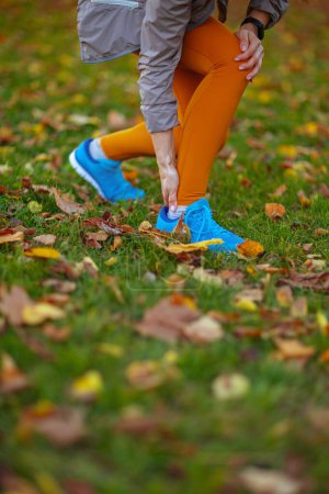 Photo for Hello autumn. Closeup on woman in fitness clothes in the park having leg pain. - Royalty Free Image