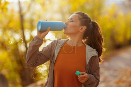 Photo for Hello autumn. trendy female in fitness clothes in the park with bottle of water. - Royalty Free Image