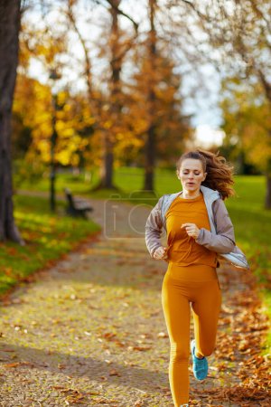 Photo for Hello autumn. middle aged woman in fitness clothes in the park running. - Royalty Free Image