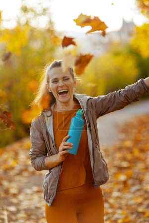 Photo for Hello autumn. happy elegant female in fitness clothes in the park with bottle of water. - Royalty Free Image
