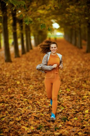 Photo for Hello autumn. trendy 40 years old woman in fitness clothes in the park jogging. - Royalty Free Image