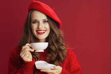 Téléchargez les photos : Joyeux Valentin. heureuse femme élégante en pull rouge et béret avec tasse à thé et soucoupe en forme de coeur. - en image libre de droit