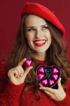 Téléchargez les photos : Happy Valentine. smiling trendy 40 years old woman in red sweater and beret with heart shaped candy box. - en image libre de droit