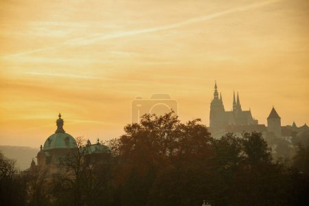 Téléchargez les photos : Paysage avec la cathédrale Saint-Vitus au coucher du soleil filmé à travers le feuillage en automne à Prague, République tchèque. - en image libre de droit