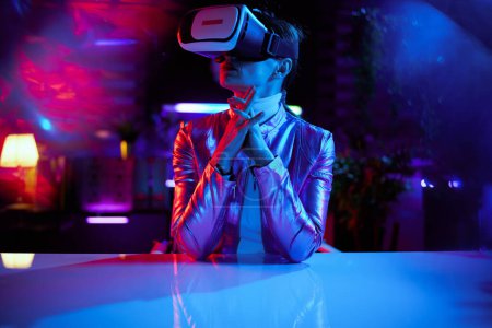 Photo for Neon metaverse futuristic concept. trendy female in virtual reality goggles in modern office working in virtual reality. - Royalty Free Image
