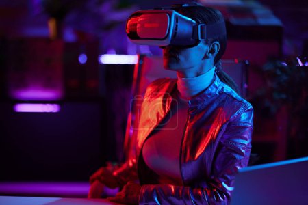 Téléchargez les photos : Neon metaverse futuristic concept. modern 40 years old woman in virtual reality goggles in modern office. - en image libre de droit