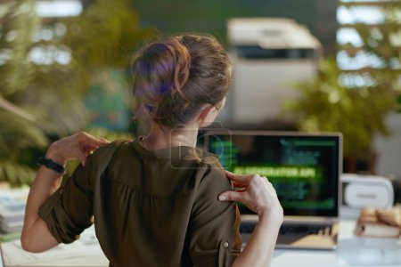 Téléchargez les photos : Vu de derrière femme moderne avec ordinateur portable ayant mal au dos dans le bureau moderne. - en image libre de droit