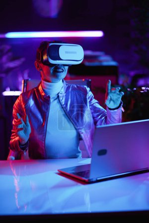 Photo for Neon metaverse futuristic concept. smiling modern woman in virtual reality goggles exploring metaverse in modern office. - Royalty Free Image