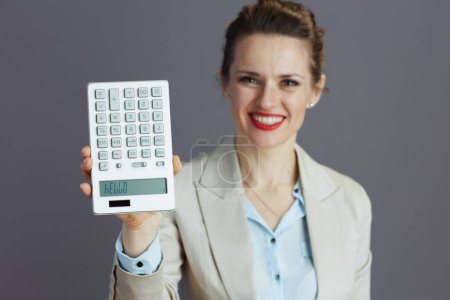 Foto de Primer plano en la sonriente mujer de negocios de mediana edad en un traje de negocios ligero con calculadora aislada sobre fondo gris. - Imagen libre de derechos