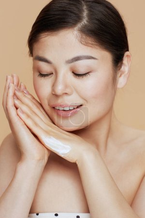 Photo for Modern asian woman with hand cream isolated on beige background. - Royalty Free Image