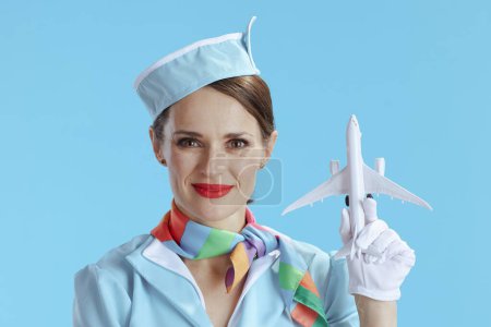 Photo for Stylish flight attendant woman isolated on blue background in blue uniform with a little airplane. - Royalty Free Image