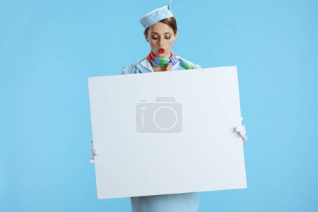 Téléchargez les photos : Surpris femme hôtesse de l'air moderne sur fond bleu uniforme bleu montrant tableau blanc. - en image libre de droit
