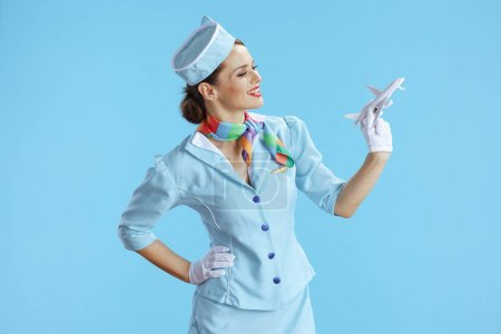 Foto de Feliz azafata moderna del aire femenino contra fondo azul en uniforme azul con un pequeño avión. - Imagen libre de derechos