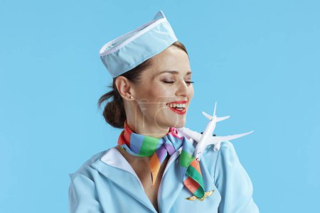 Foto de Feliz elegante azafata de aire femenino aislado sobre fondo azul en uniforme azul con un pequeño avión. - Imagen libre de derechos